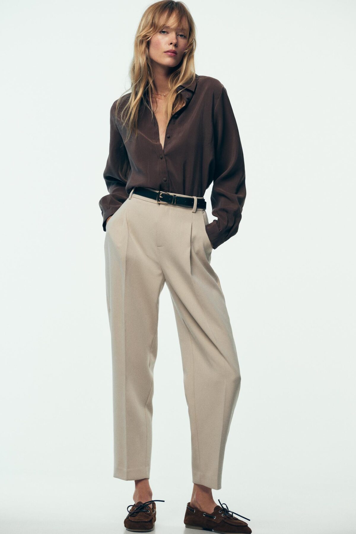 09929222743 p شلوار «darted trousers with belt» از zara در طیف رنگی شیک و همه‌پسند—light camel، مشکی و oyster-white—عرضه می‌شود. طراحی آن با کمر بلند (high-waist) و قد مچی (ankle-length) با یک کمربند هماهنگ علاوه بر جلوه مدرن، تناسب و استیل را ارتقاء می‌دهد. دوخت سه‌بعدی (darts) در جلو، فرم زیبا و ساختار دقیق به این شلوار می‌بخشدجیب‌های کاربردی در جلو و جیب‌های فیک با درب پشت (false flap pockets) حس طراحی خاص همچون کت و شلوار را به ارمغان می‌آورد. فرم پا به‌صورت straight leg است که ظاهری کلاسیک و ارتجاع‌پذیر دارد. جایگاه بسته‌شدن در جلو با زیپ، دکمه داخلی و قلاب فلزی تضمین‌گر راحتی و ثبات در تنظیم‌اند. ترکیب پارچه‌ای از ۷۴٪ پلی‌استر، ۲۰٪ ویسکوز و ۶٪ الاستان، بافتی نرم و کشسان فراهم کرده است—ایده‌آل برای استفاده روزمره و موقعیت‌های رسمی.